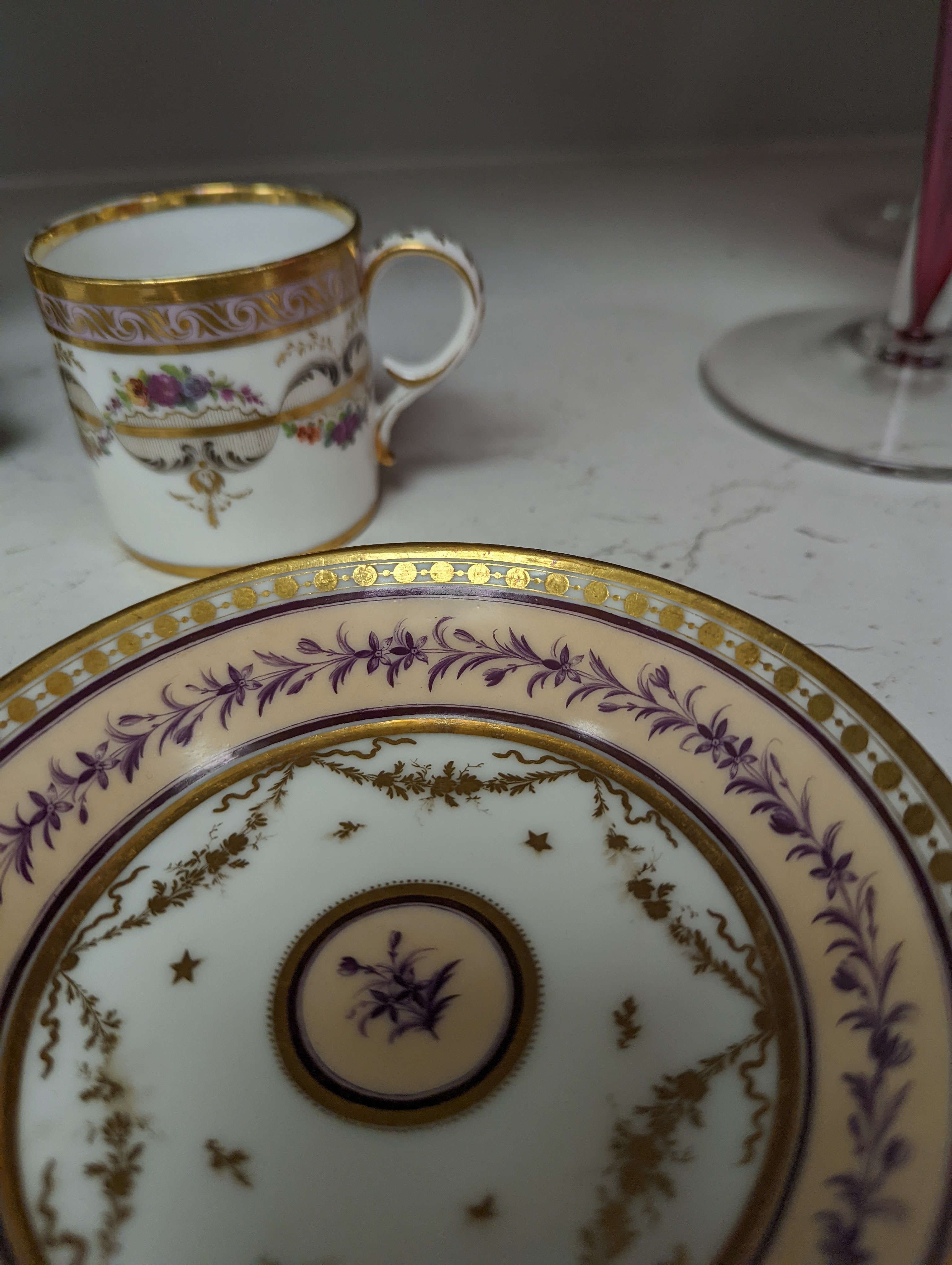 A Duc d'Angouleme coffee can and saucer painted with a puce chain of leaves on a salmon coloured ground and another painted with a flower chain, black feather and a gilt line, latter with stencilled red mark 'Manuf de M